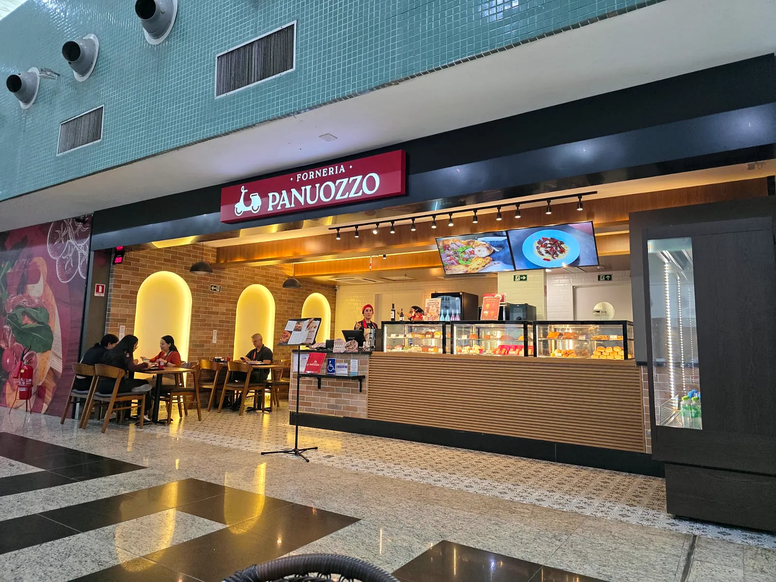 Forneria Panuozzo no Aeroporto Internacional de Manaus: letreiro vermelho, tijolos com nichos iluminados e balcão em madeira.