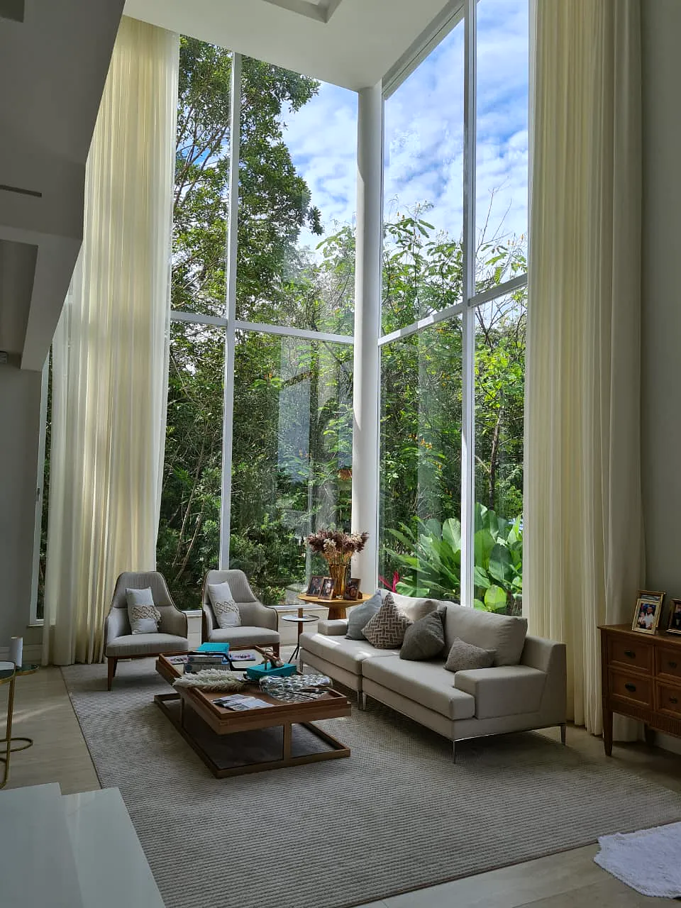 Sala com pé-direito duplo, janelas do piso ao teto e vista para a mata.