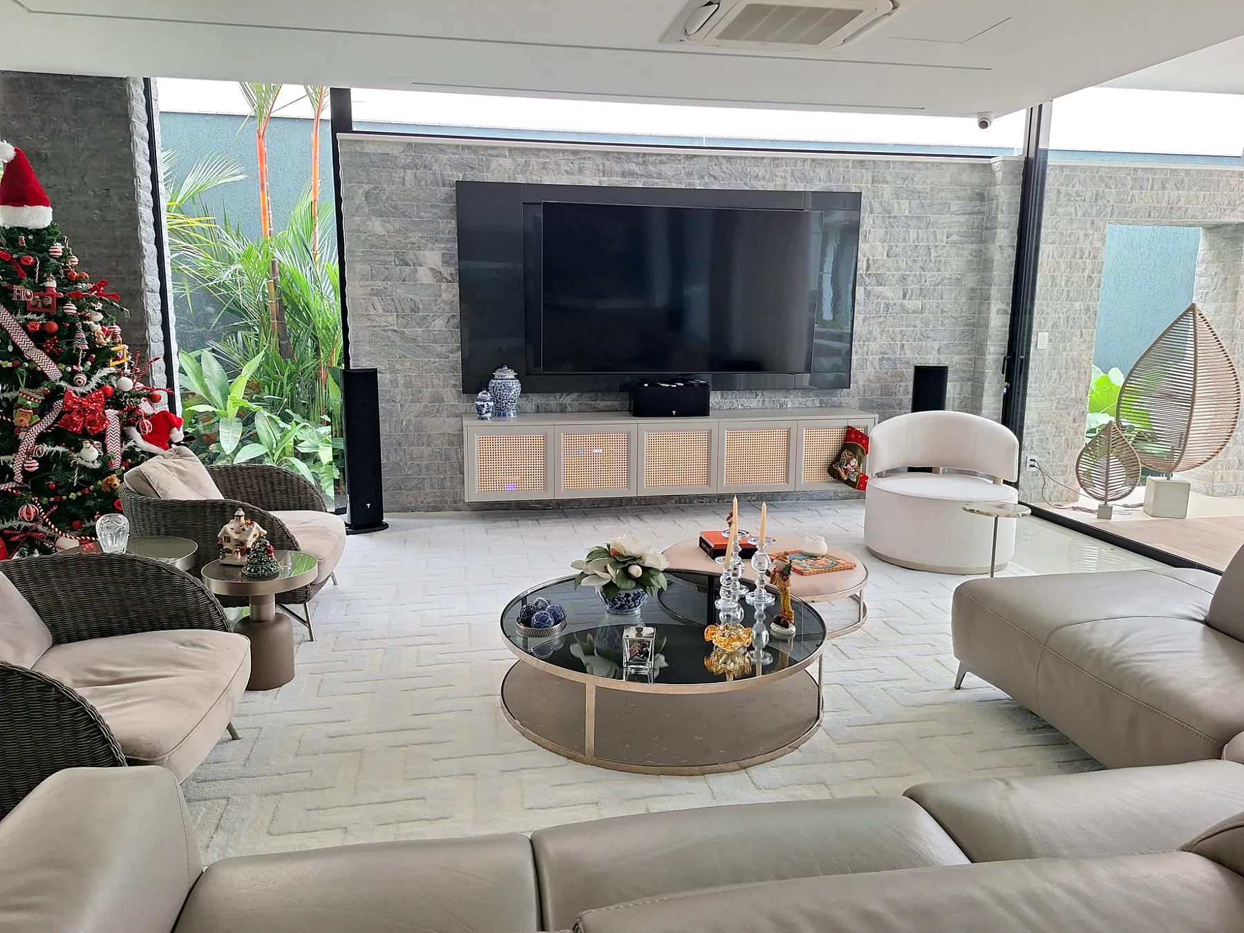 Sala de estar com painel em pedra, móveis claros e jardim tropical ao redor.